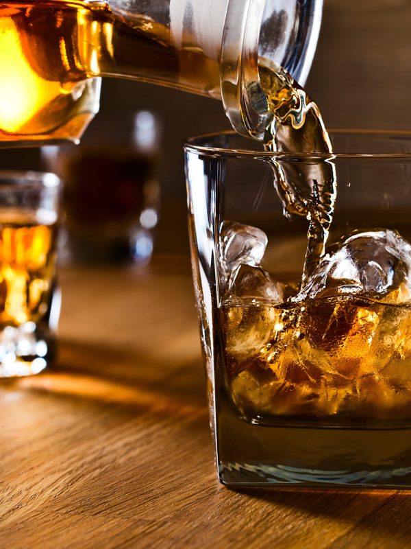 Bourbon being poured from a bottle into a glass with ice+